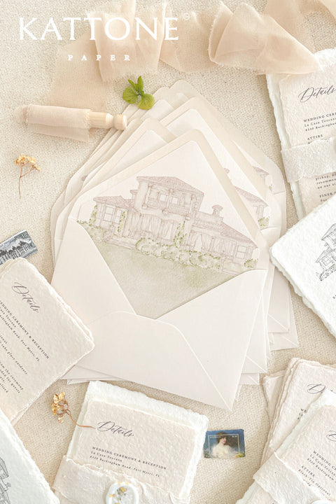 Wedding envelopes with watercolor venue envelope liners styled on neutral linen with handmade paper details and fine art stationery elements.