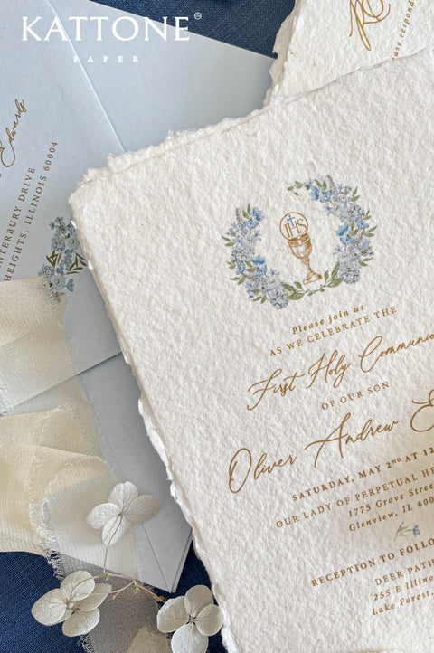 Close up of textured handmade paper invitation with gold lettering and delicate religious illustration.