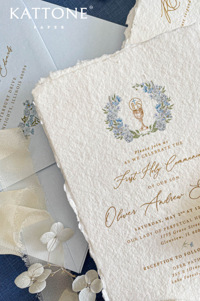 Close up of textured handmade paper invitation with gold lettering and delicate religious illustration.