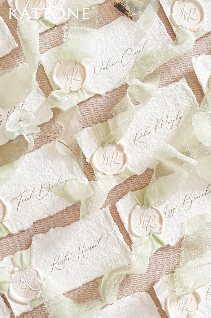 Luxury handmade paper wedding place cards featuring deckled edge cotton paper, elegant calligraphy guest names, sage chiffon ribbon, and wax seal detailing.