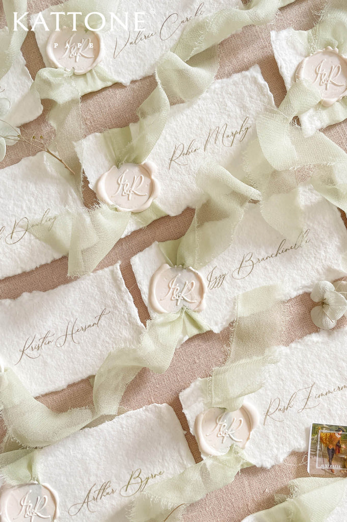 Luxury handmade paper wedding place cards featuring deckled edge cotton paper, elegant calligraphy guest names, sage chiffon ribbon, and wax seal detailing.