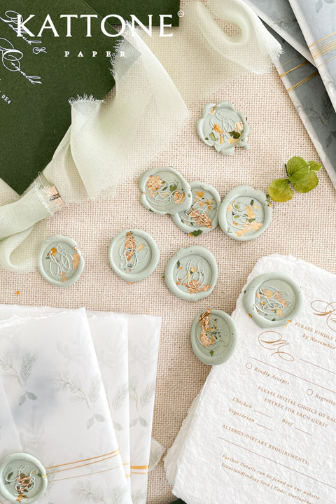 Soft sage wax seals accented with delicate flecks of gold leaf, designed to elevate wedding invitations, envelopes, and fine stationery with an organic, timeless finish. Each seal is individually hand-poured, creating subtle variations that make every piece feel artisanal and one of a kind. Perfect for romantic, botanical, and modern celebrations seeking a refined yet natural detail.
