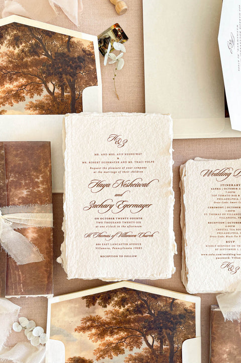 Luxury handmade paper wedding invitation suite featuring deckled edge cotton paper, elegant calligraphy typography, custom scenic vellum wraps, and warm autumn-inspired fine art wedding stationery.