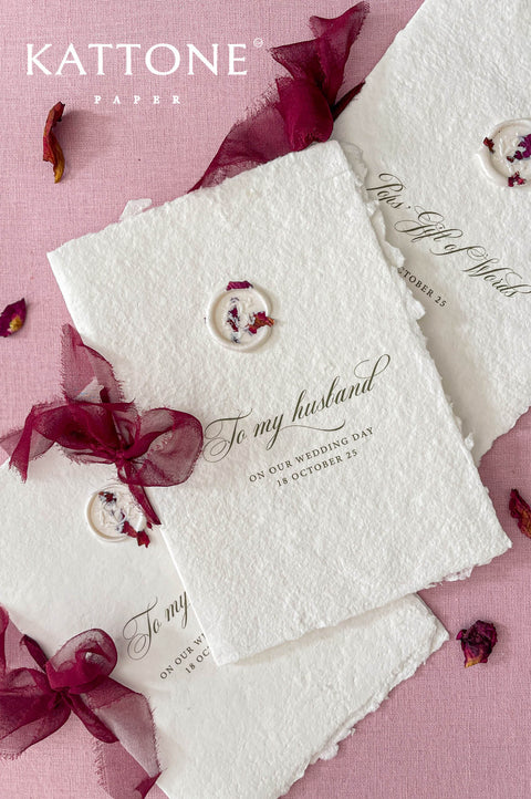 Handmade paper wedding vow booklet with deckled edges, elegant calligraphy text, and wax seal on blush background