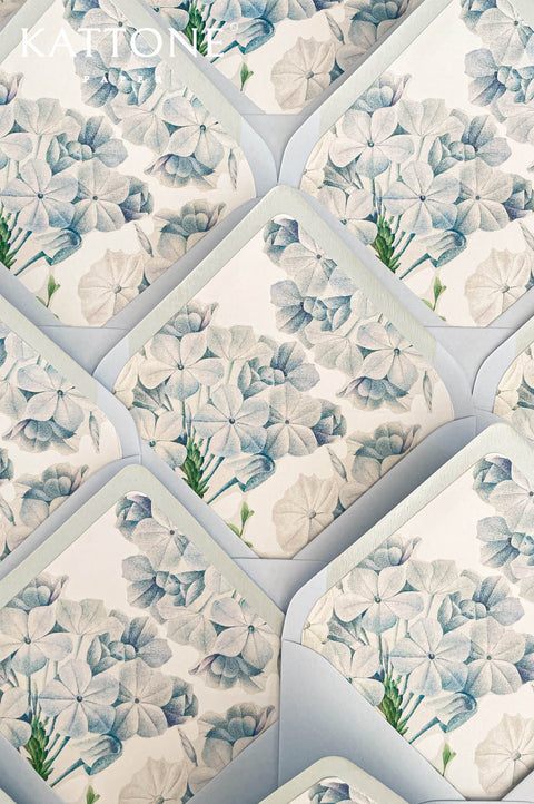 Light blue wedding envelopes with soft matte finish and delicate hydrangea-style watercolor floral liners in blue and green tones, paired with handmade cotton paper save the date cards.