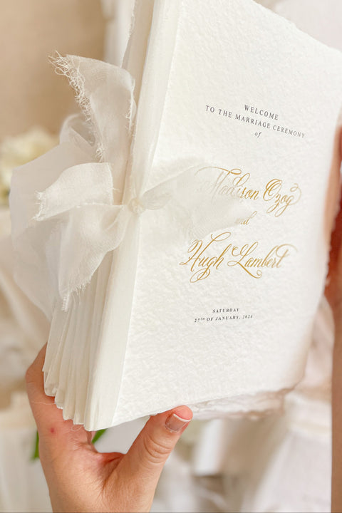 A beautifully handcrafted wedding program made from premium cotton paper, designed to elevate your ceremony with soft texture, timeless script, and a romantic ribbon finish. Each program is thoughtfully created to introduce your guests to the most meaningful moments of your day, blending fine-art aesthetics with the warmth of handmade craftsmanship. Ideal for classic, garden, or luxury weddings, it delivers a refined first impression that sets the tone for a heartfelt celebration.