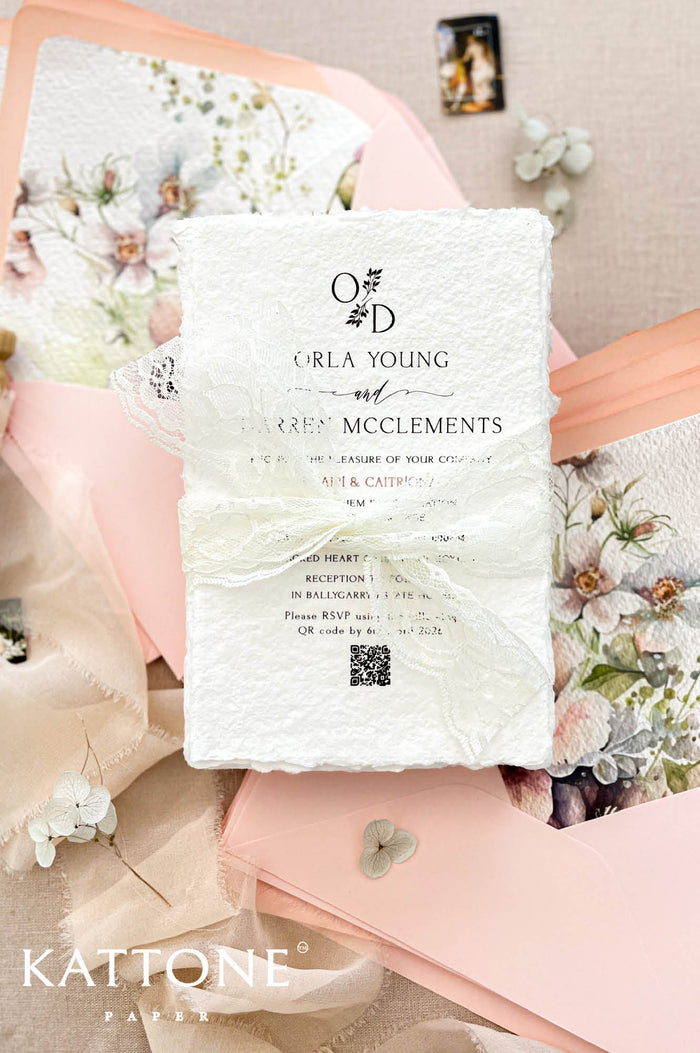 Luxury handmade cotton paper wedding invitation with deckled edges wrapped in ivory lace ribbon, styled with blush pink envelopes and watercolor floral envelope liners.