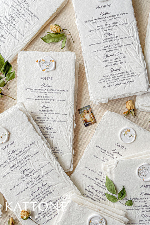 Elevate your wedding table with our embossed handmade paper menus, where timeless craftsmanship meets modern refinement. Each menu is printed on 100% cotton handmade paper with delicate deckled edges and a subtle botanical embossing, creating a tactile experience of understated luxury. Finished with an elegant floral wax seal personalized for each guest, these menus add an exquisite fine-art touch to your reception decor.