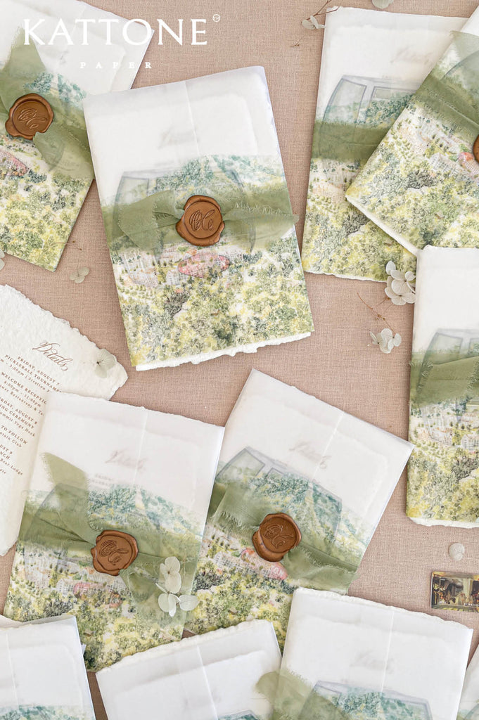 Soft translucent vellum wrap printed with custom watercolor landscape artwork layered over handmade paper invitations, creating dimension, softness, and elevated luxury presentation.