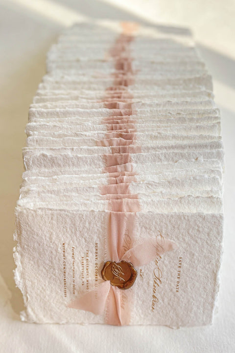 Announce your wedding day with effortless elegance through our handmade paper Save the Date cards, a perfect blend of romance and artisanal craftsmanship. Printed on luxury 100% cotton paper with soft deckled edges, each piece is wrapped in a delicate blush silk ribbon and finished with a hand-pressed wax seal, creating a timeless keepsake that captures the essence of fine-art stationery.