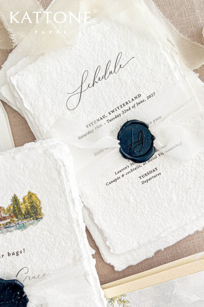 Detailed overhead photograph of a luxury birthday celebration schedule printed on ivory handmade paper with organic deckled edges. Elegant black calligraphy, classic typography, a sheer ivory ribbon and a personalized navy blue wax seal complete the design, accompanied by coordinating watercolor invitation cards and an illustrated Swiss lakeside envelope liner on natural beige linen.