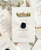 Styled overhead photograph of luxury handmade paper birthday invitations for a Swiss lakeside celebration. The ivory invitation features custom watercolor artwork of a historic waterfront hotel, an ivory ribbon and navy blue personalized wax seal, surrounded by matching schedule and details cards, watercolor envelope liners illustrating Lake Lucerne and the Swiss Alps, and soft beige linen fabric.