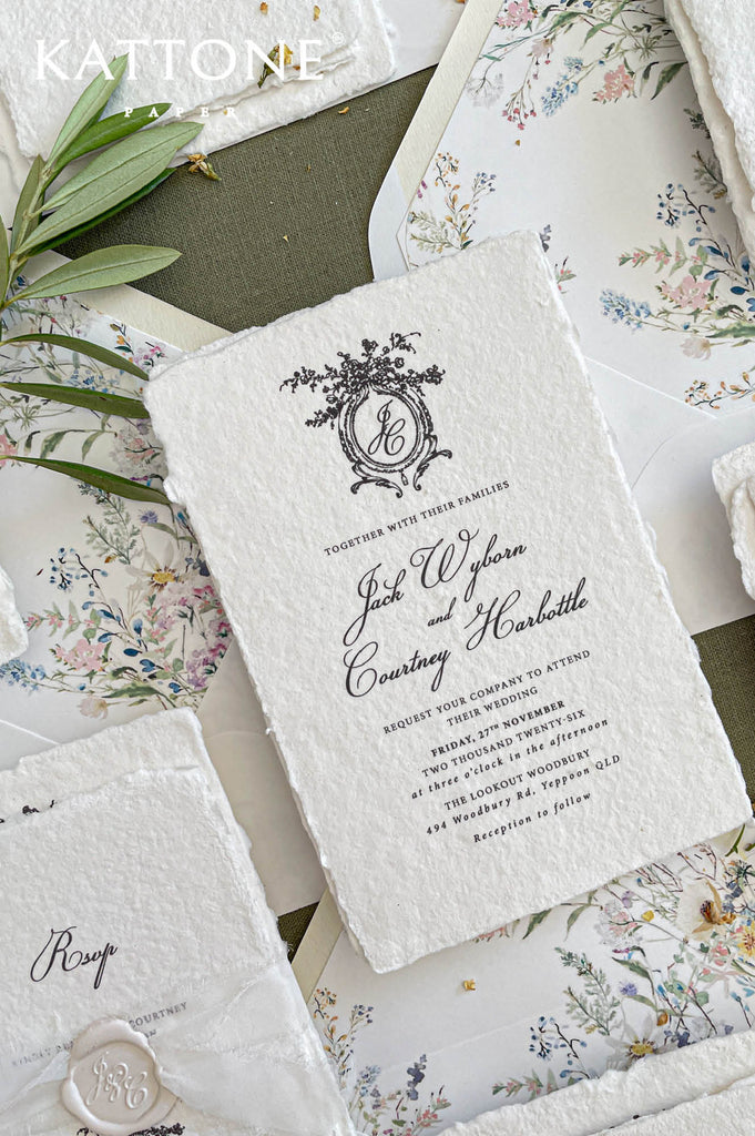 Close up of textured handmade cotton paper invitation showing organic deckled edges, vintage crest monogram and elegant typography.