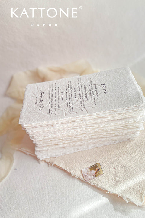 These embossed handmade paper wedding menus embody the essence of refined elegance and timeless artistry. Each piece is crafted from 100% cotton rag paper, known for its organic texture and signature deckled edges that add an artisanal, heirloom feel. The design features delicate blind embossing of botanical motifs, adding soft dimension and sophistication, while luxurious typography in classic ink beautifully contrasts the natural paper’s tactile surface.
