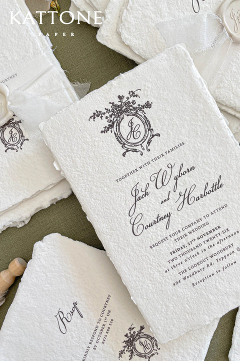 Close up of textured handmade cotton paper invitation showing organic deckled edges, vintage crest monogram and elegant typography.