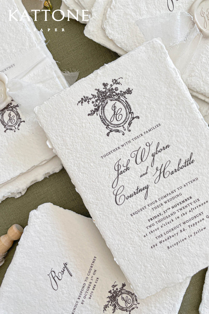 Close up of textured handmade cotton paper invitation showing organic deckled edges, vintage crest monogram and elegant typography.