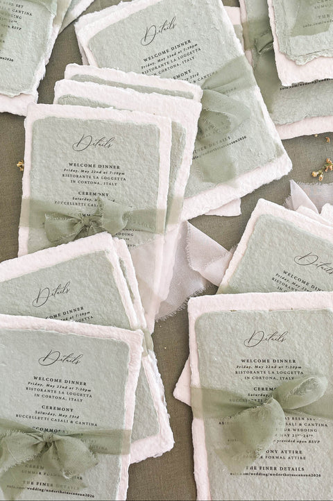 Sage green hand-torn silk ribbon tied around handmade wedding invitation adding soft movement and organic texture.