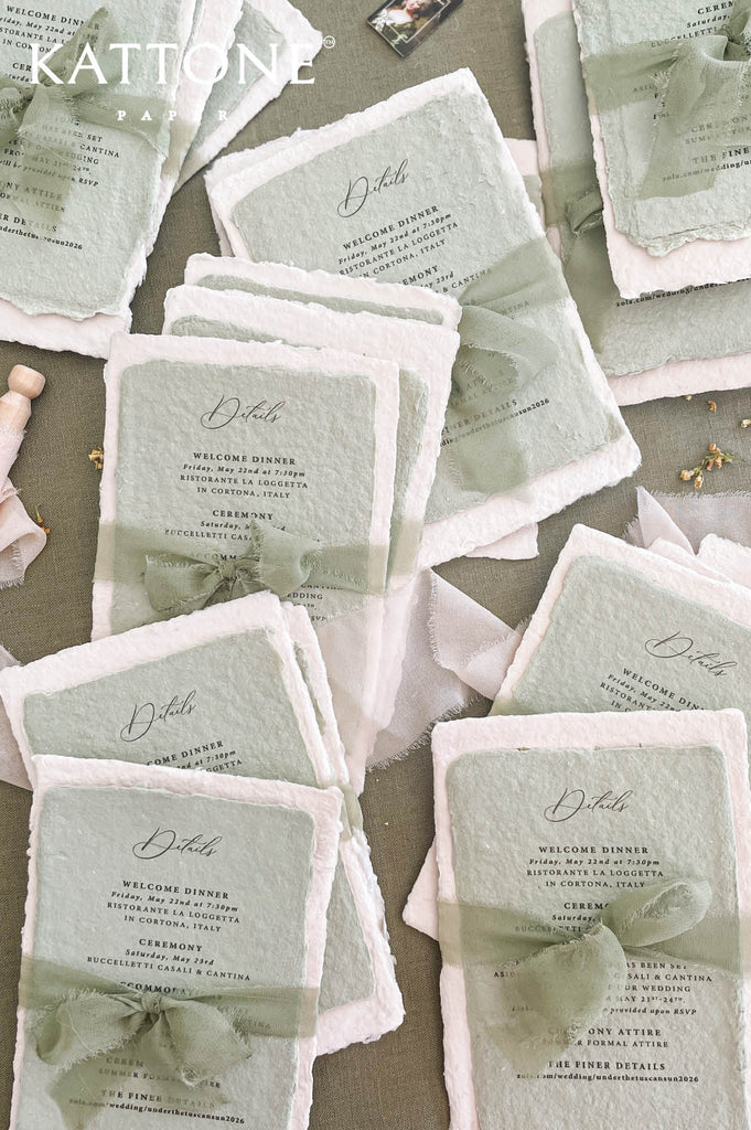 Sage green hand-torn silk ribbon tied around handmade wedding invitation adding soft movement and organic texture.