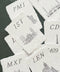 Handmade paper wedding place cards with deckled edges featuring architectural landmark illustrations and elegant serif initials.