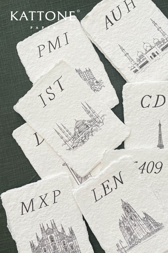 Handmade paper wedding place cards with deckled edges featuring architectural landmark illustrations and elegant serif initials.