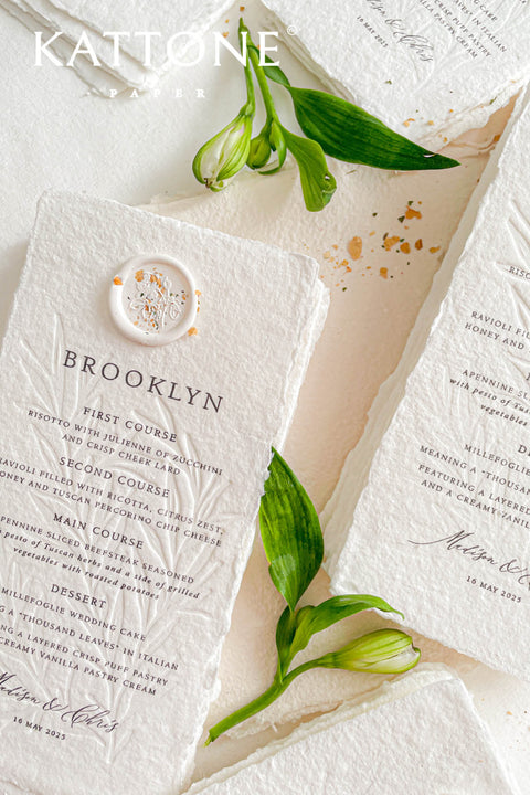 These embossed handmade paper wedding menus embody the essence of refined elegance and timeless artistry. Each piece is crafted from 100% cotton rag paper, known for its organic texture and signature deckled edges that add an artisanal, heirloom feel. The design features delicate blind embossing of botanical motifs, adding soft dimension and sophistication, while luxurious typography in classic ink beautifully contrasts the natural paper’s tactile surface.