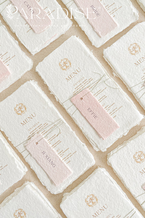 These handmade paper wedding menus capture the essence of fine art romance and luxury craftsmanship. Each menu is meticulously created from 100% cotton rag paper, known for its naturally soft texture and deckled edges, creating an heirloom-quality keepsake for your wedding day. The design features a custom gold monogram crest printed in elegant metallic foil, paired with refined typography and delicate blush pink name tags, tied gracefully with natural twine for a personal, layered touch.