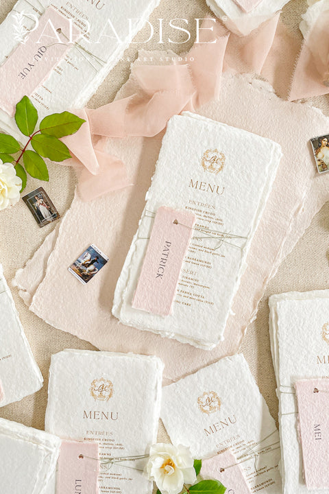 These handmade paper wedding menus capture the essence of fine art romance and luxury craftsmanship. Each menu is meticulously created from 100% cotton rag paper, known for its naturally soft texture and deckled edges, creating an heirloom-quality keepsake for your wedding day. The design features a custom gold monogram crest printed in elegant metallic foil, paired with refined typography and delicate blush pink name tags, tied gracefully with natural twine for a personal, layered touch.