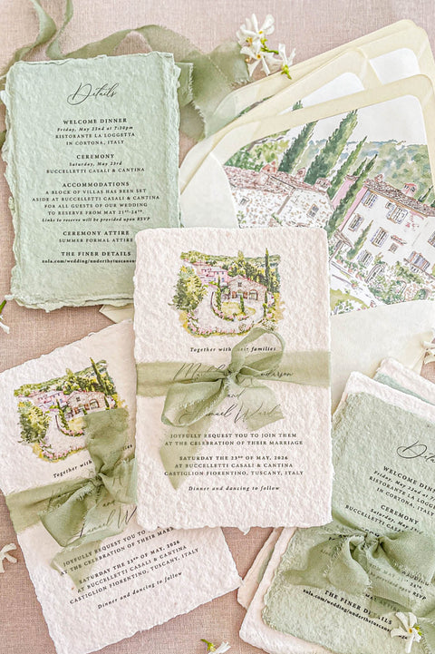 Handmade cotton paper wedding invitation with deckled edges and watercolor Tuscan villa illustration, styled with sage green silk ribbon and matching envelope liners.