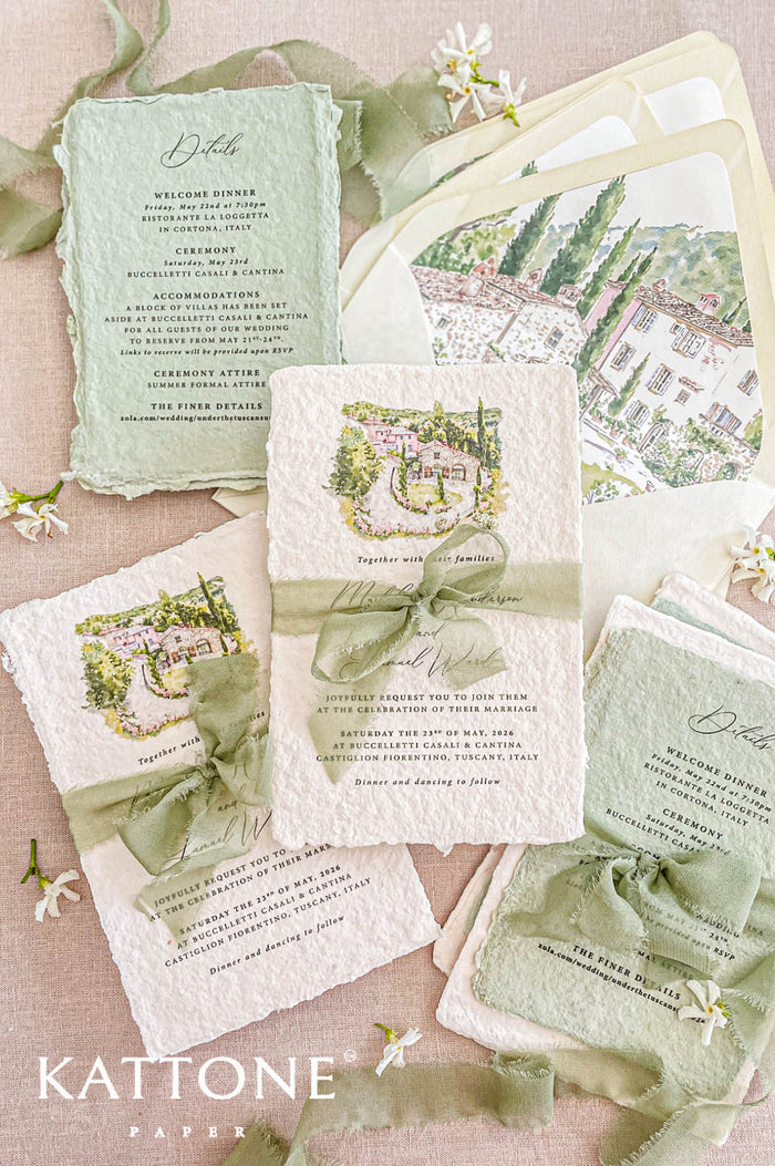 Handmade cotton paper wedding invitation with deckled edges and watercolor Tuscan villa illustration, styled with sage green silk ribbon and matching envelope liners.