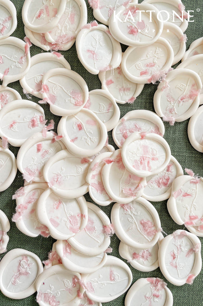 Close-up of ivory wax seal featuring pressed pink botanicals and embossed floral design.