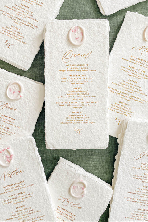 Stacked handmade paper wedding menus with deckled edges and wax seal details for elegant table settings.