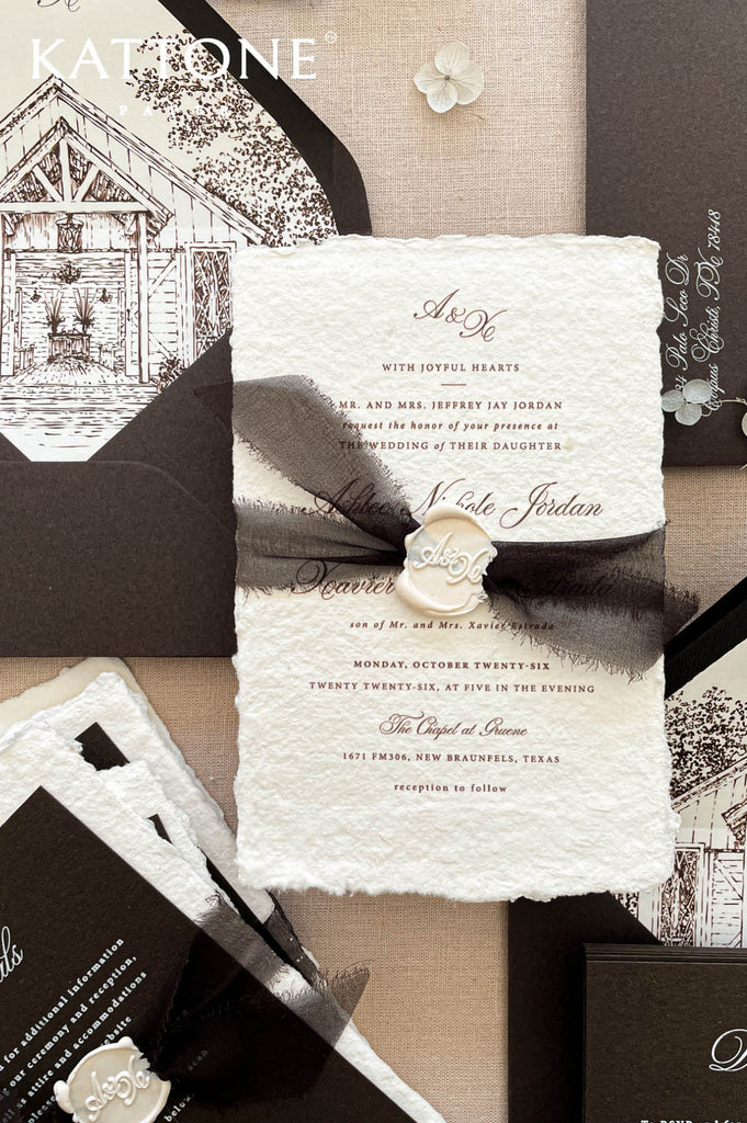 Luxury handmade paper wedding invitation suite with deep espresso envelopes, chapel illustration liners, black ribbon, and wax seal.