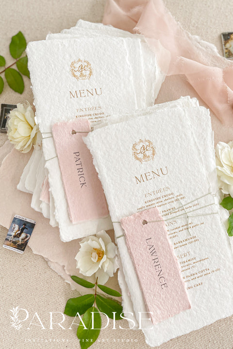 These handmade paper wedding menus capture the essence of fine art romance and luxury craftsmanship. Each menu is meticulously created from 100% cotton rag paper, known for its naturally soft texture and deckled edges, creating an heirloom-quality keepsake for your wedding day. The design features a custom gold monogram crest printed in elegant metallic foil, paired with refined typography and delicate blush pink name tags, tied gracefully with natural twine for a personal, layered touch.