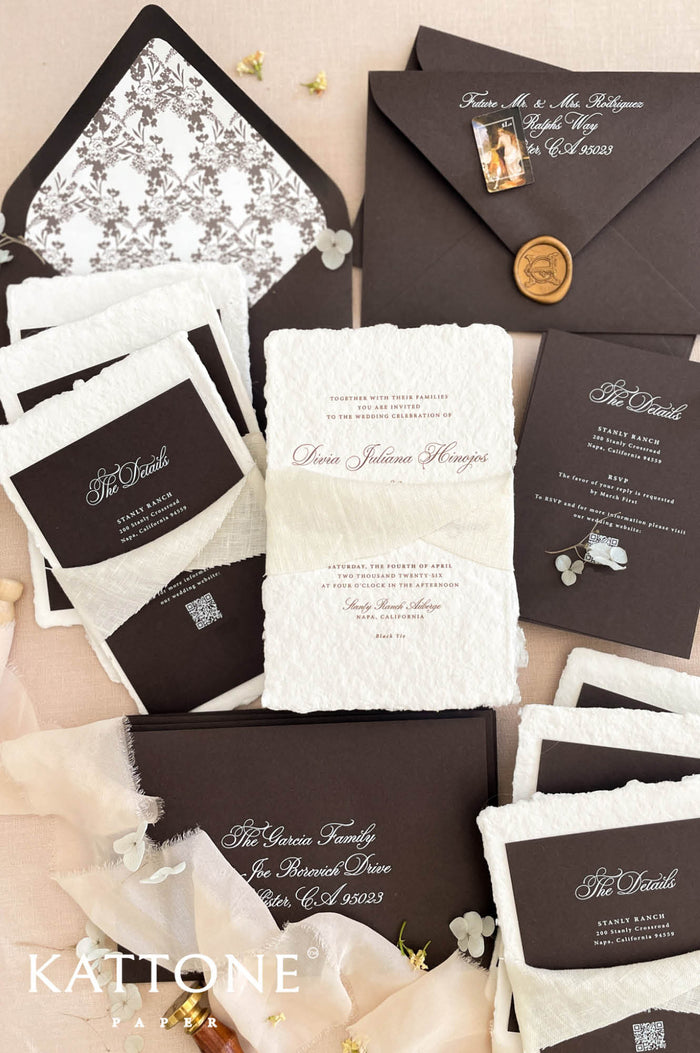 Handmade cotton paper wedding invitation with deckled edges and elegant script typography, styled with ivory chiffon ribbon, dark brown inserts and matching envelopes.