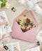 Rose pink wedding envelopes with floral envelope liners styled on neutral linen with silk ribbon, floral accents, and fine art stationery details.