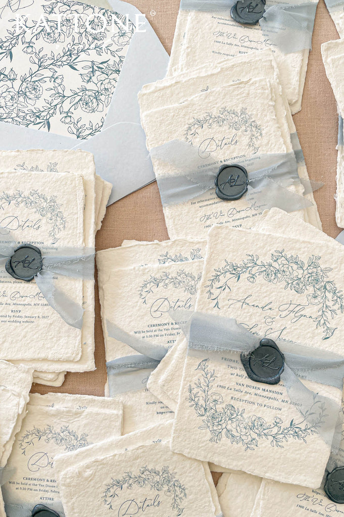 Elegant handmade paper wedding invitation with deckled edges featuring refined typography and romantic blue floral artwork.