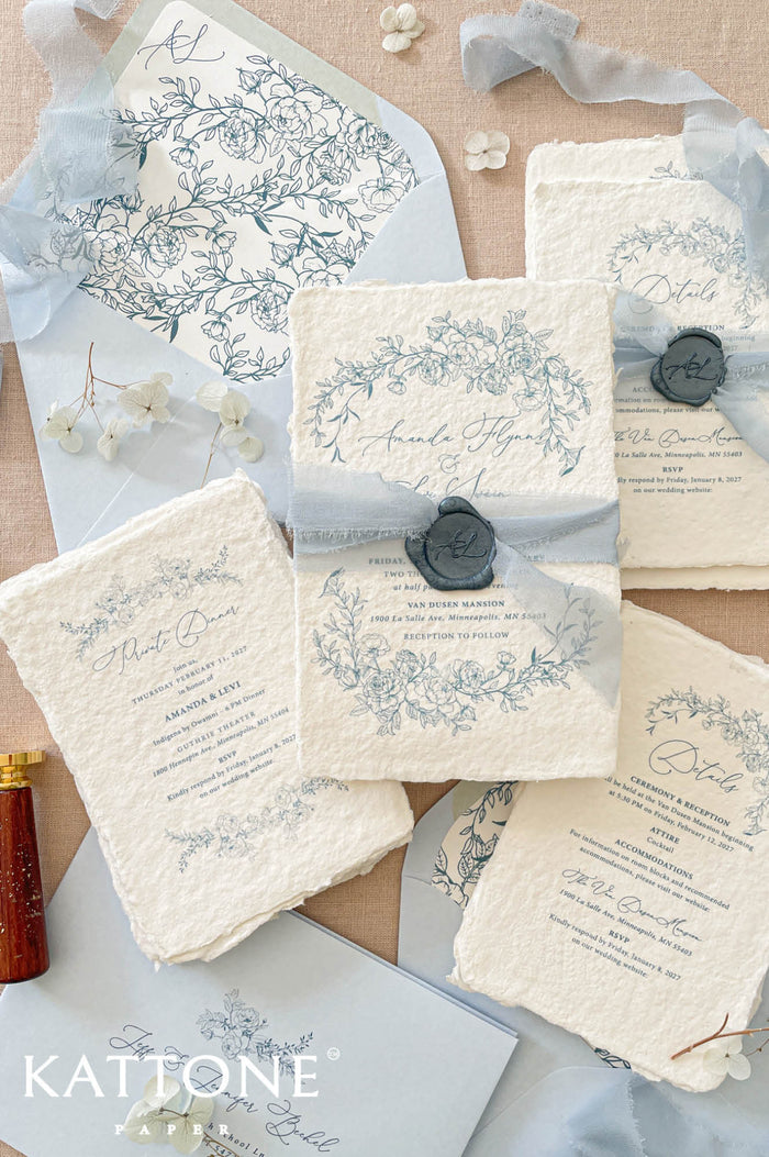 Luxury handmade paper wedding invitation suite featuring deckled edge cotton paper, delicate blue floral illustrations, powder blue chiffon ribbon, wax seal accents, and coordinating blue wedding stationery.