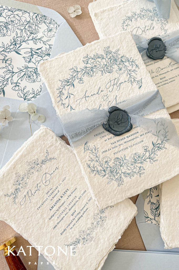 Romantic flat lay of luxury wedding stationery showcasing handmade paper invitations, floral envelope liners, chiffon ribbon styling, and coordinating inserts.