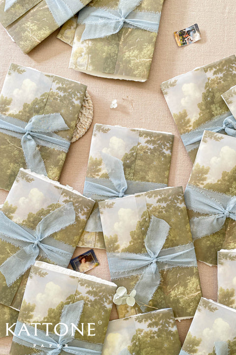 Soft translucent vellum wrap printed with scenic landscape artwork layered over handmade paper invitations, creating depth, texture, and elevated luxury presentation.