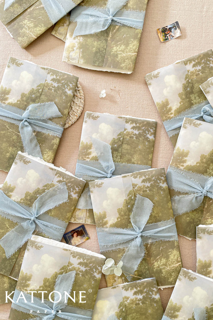 Soft translucent vellum wrap printed with scenic landscape artwork layered over handmade paper invitations, creating depth, texture, and elevated luxury presentation.