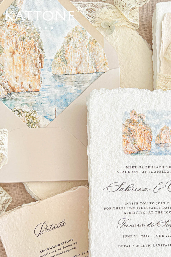 Close-up of a luxury blush wedding envelope opened to reveal a custom watercolor liner illustrating the Faraglioni of Scopello in Sicily, with golden limestone cliffs, soft coastal greenery, and tranquil blue Mediterranean waters. Styled alongside a white deckle-edge handmade paper wedding invitation, ivory lace ribbon, and a warm beige wedding details card for an elegant Italian coastal destination wedding.