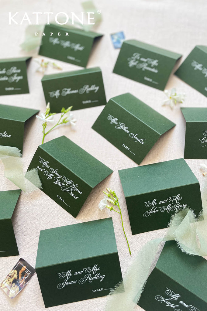 Wedding reception table décor featuring folded green place cards with elegant typography.