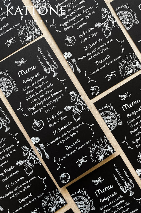Flat lay of whimsical black wedding menus arranged with hand-drawn illustrations for a modern tablescape.