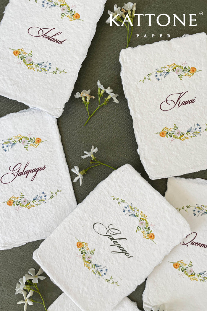Watercolor floral handmade paper place cards featuring soft deckled edges, hand-torn cotton paper, and elegant calligraphy table names framed by delicate botanical florals in muted garden tones.