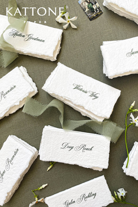 Handmade paper wedding place cards with deckled edges and calligraphy names on a neutral linen background.