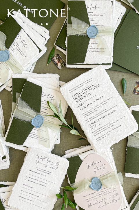 Flat lay of luxury wedding stationery including handmade paper invitations, RSVP cards, details cards, and forest green envelopes.