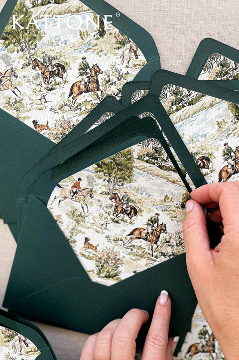 Stacked forest green envelopes with illustrated watercolor liners, creating a refined and artistic wedding stationery presentation.