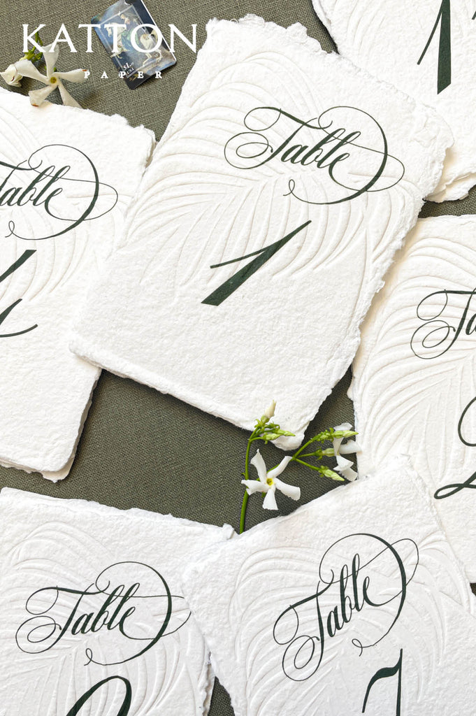 Close-up of embossed handmade paper table number showing pressed texture and deckle edge detail.