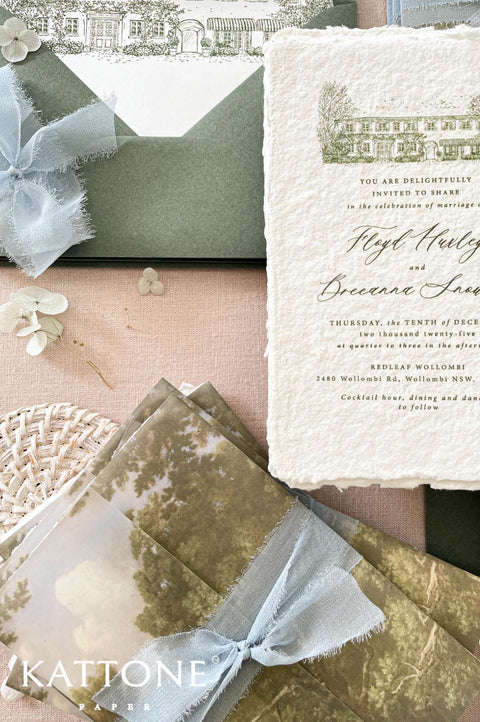 Soft translucent vellum wrap printed with scenic landscape artwork layered over handmade paper invitations, creating depth, texture, and elevated luxury presentation.