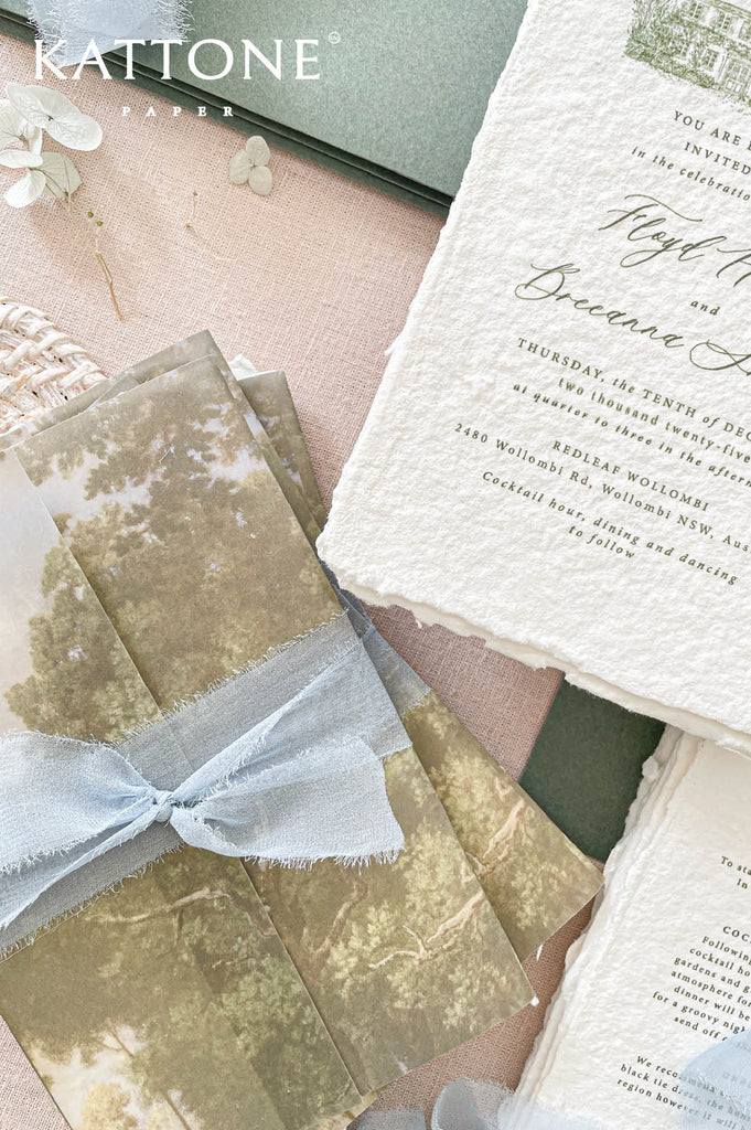 Soft translucent vellum wrap printed with scenic landscape artwork layered over handmade paper invitations, creating depth, texture, and elevated luxury presentation.